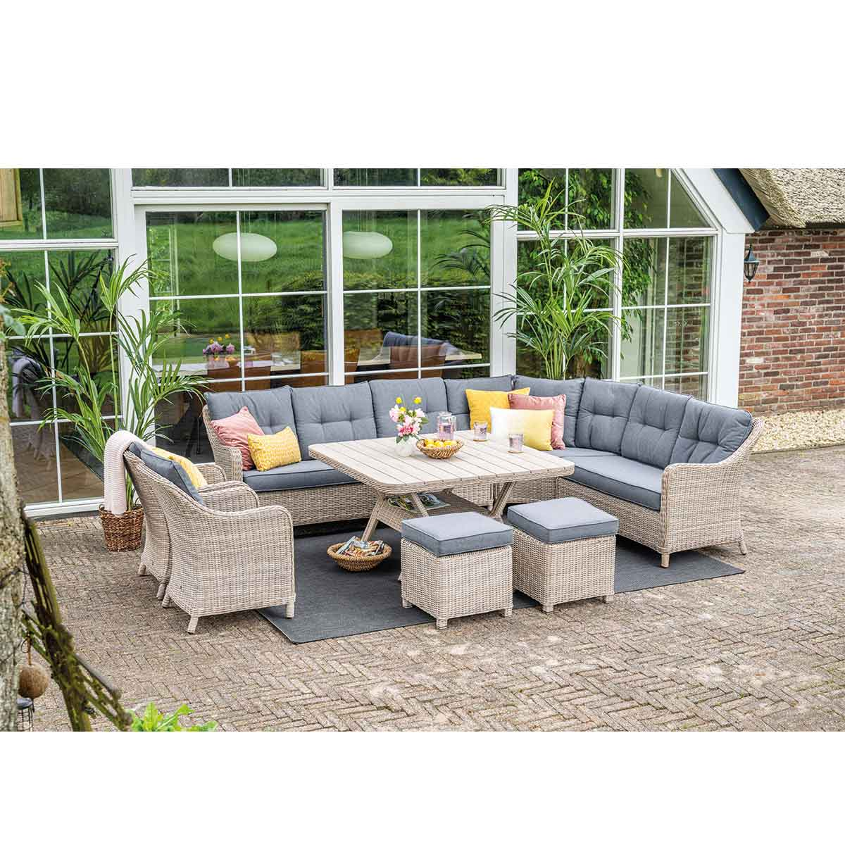 Outdoor furniture set with sofas, chairs, and ottomans, arranged on patio with plants and windows.