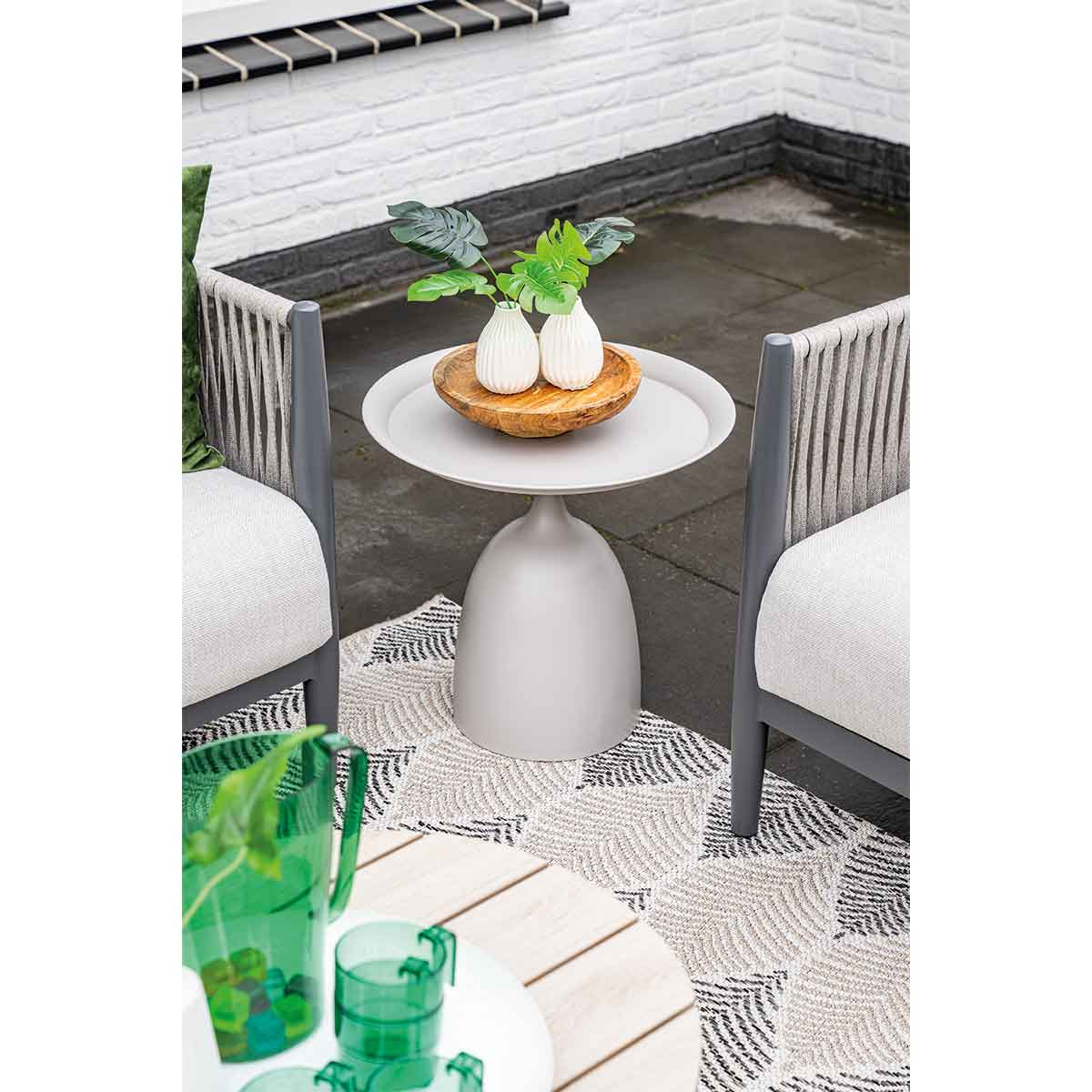 Table d'appoint avec fleurs et décorations. Table grise claire, vases blancs et bol en bois sur tapis à motifs.