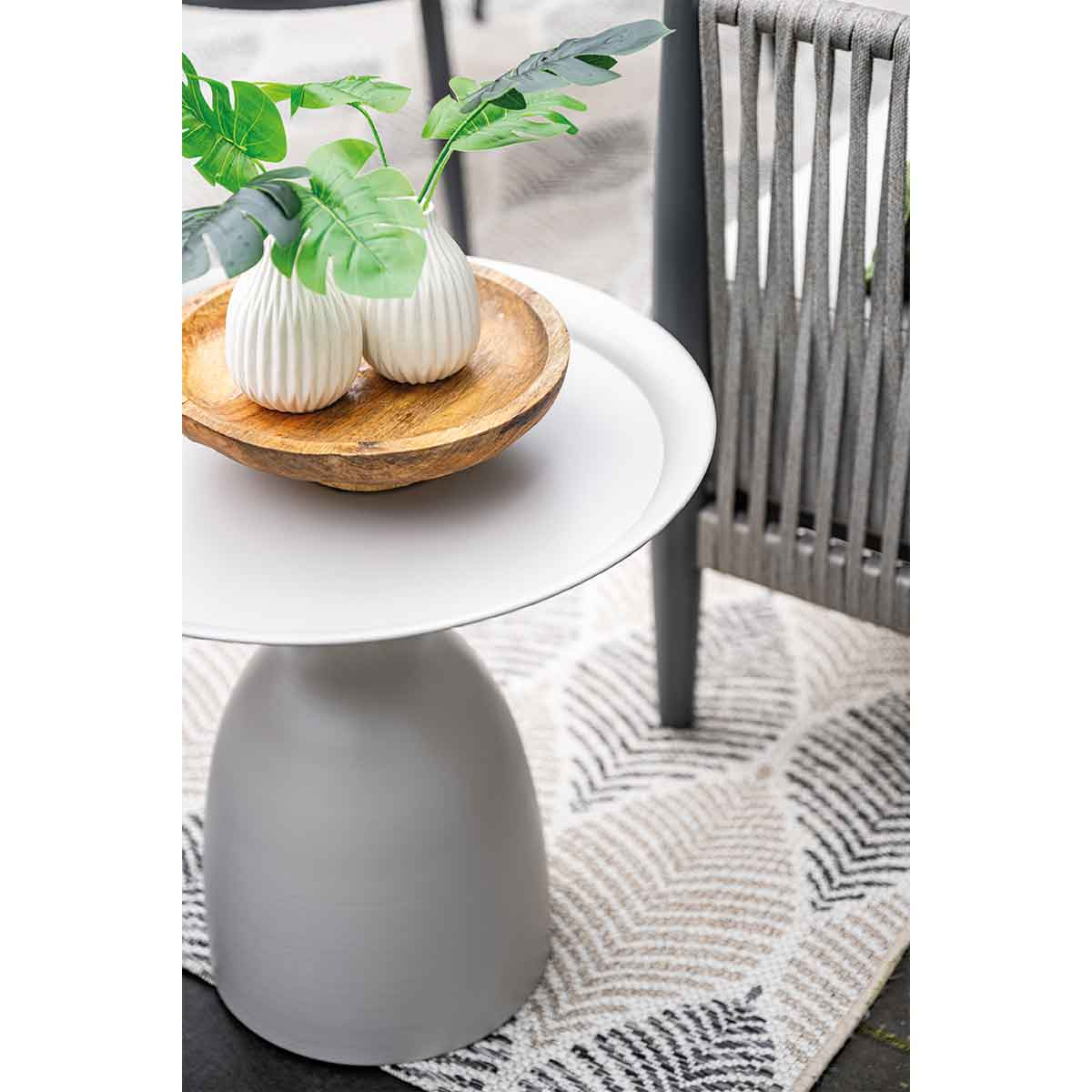 Table blanche avec objets. Bol en bois, plantes vertes, tapis et chaise.