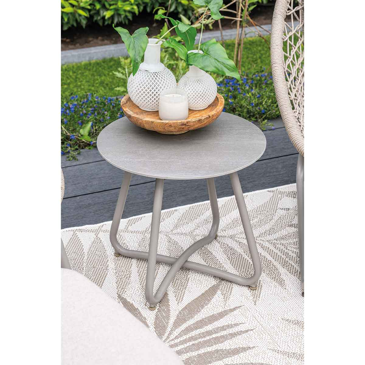 Ronde grijze tafel met decoratie op een kleed. Groene achtergrond en blauwe bloemen.