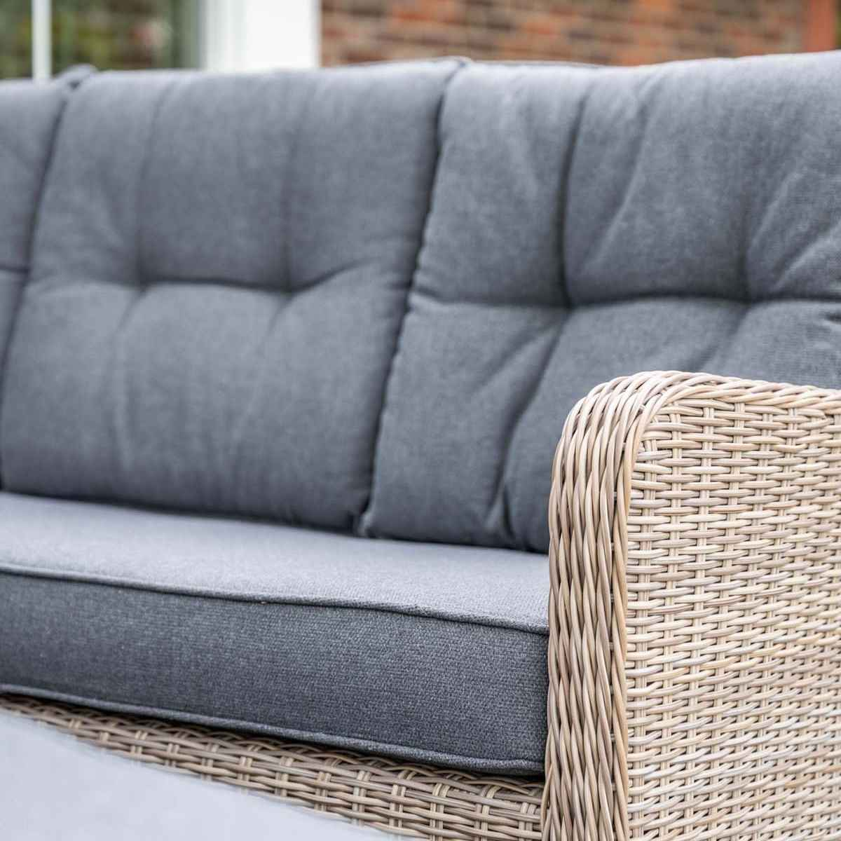 A grey sofa with wicker armrests. The cushions are grey. The sofa is on a patio.
