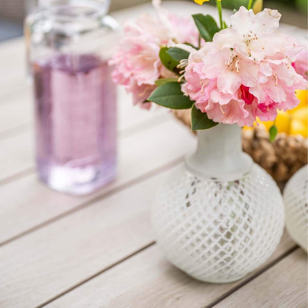 Pink flowers in a white vase. Jar of pink liquid in the background.