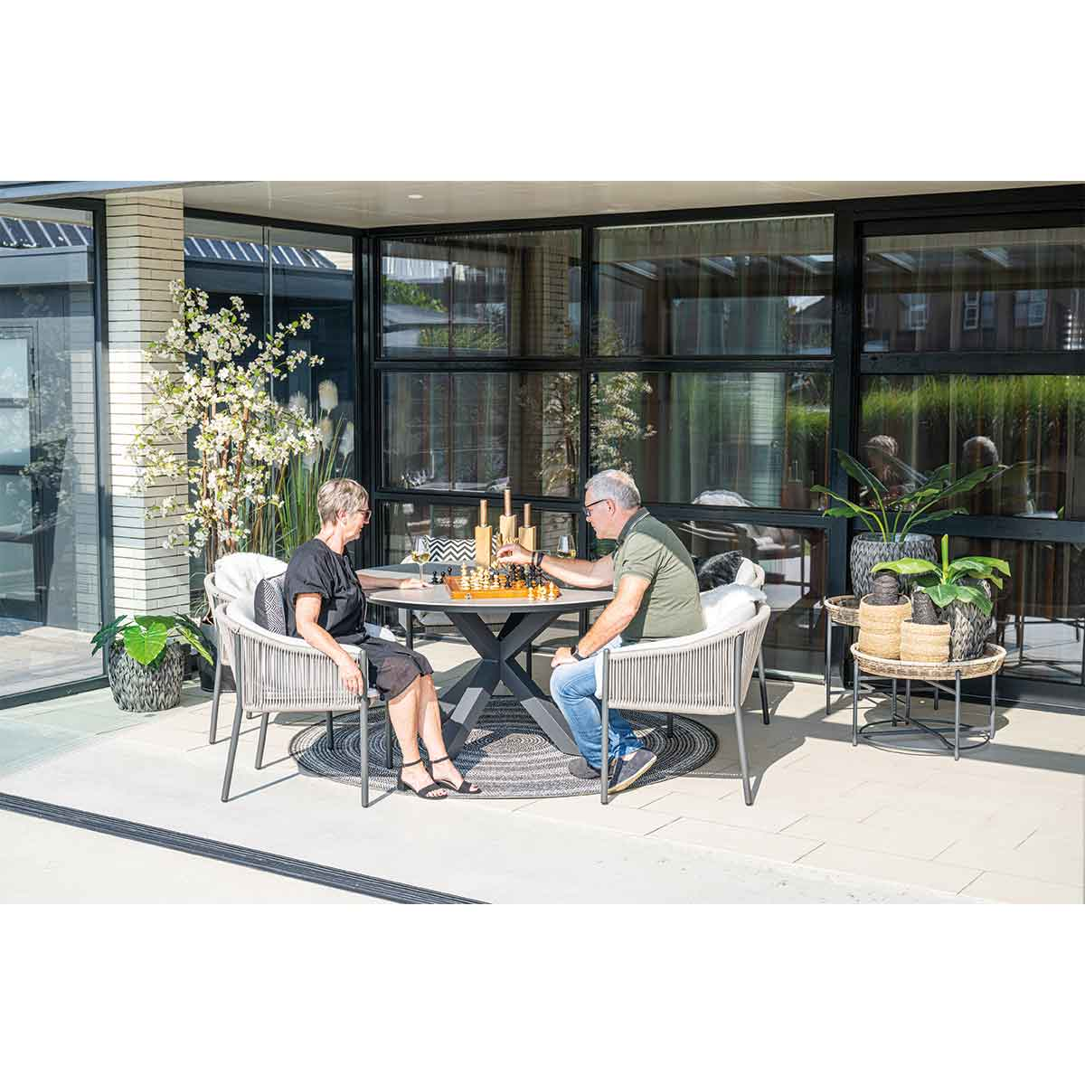 Two people playing chess at a round table on a patio.