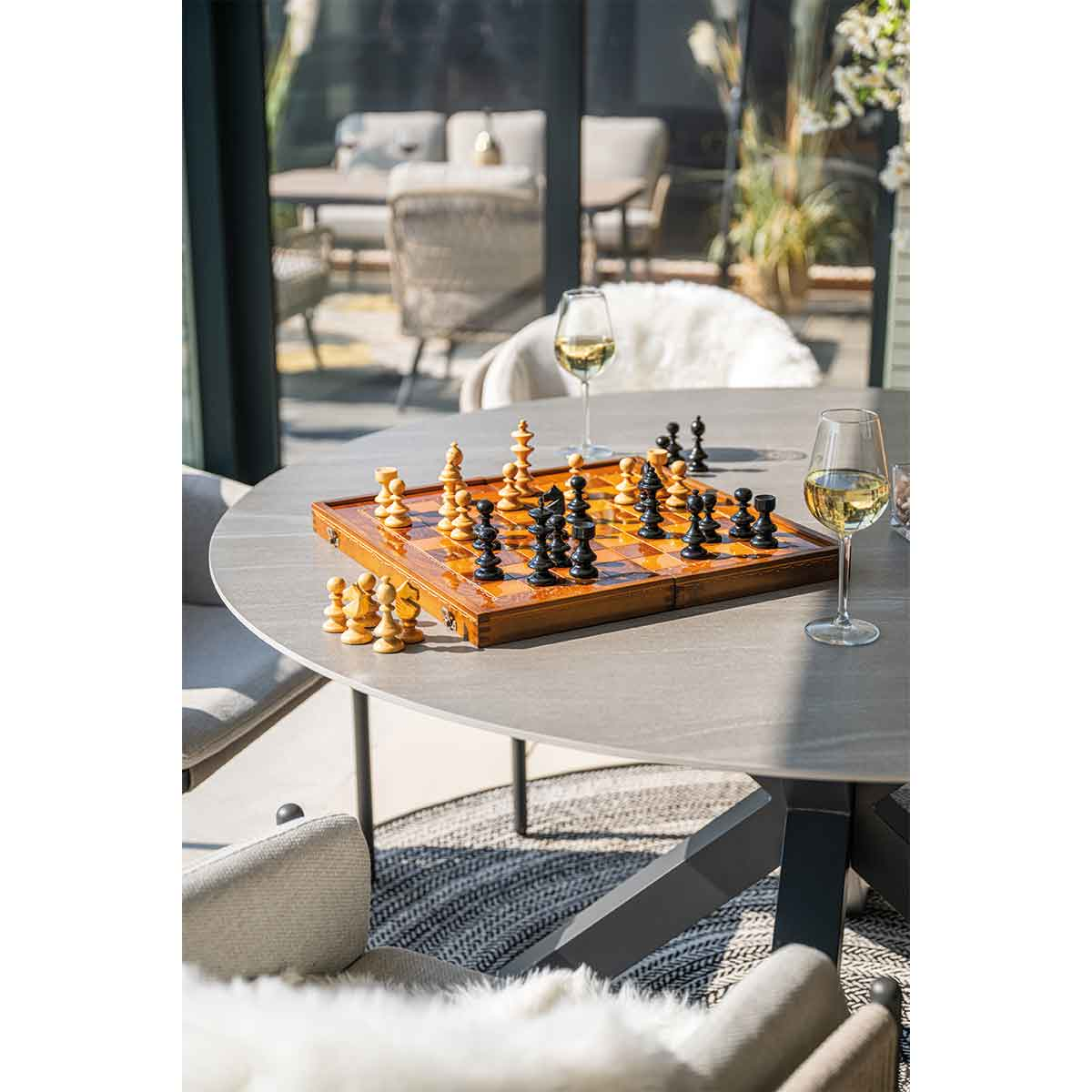A chess board with pieces set up on a gray table with two glasses of wine.
