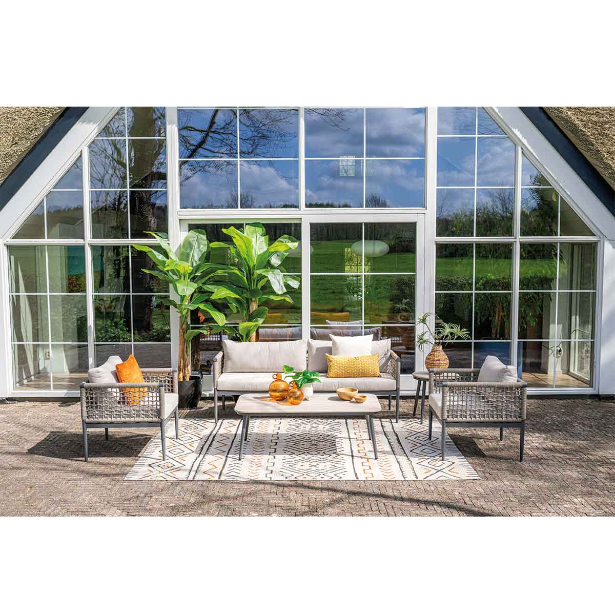 Outdoor patio scene with large windows, furniture, plants, and a patterned rug.