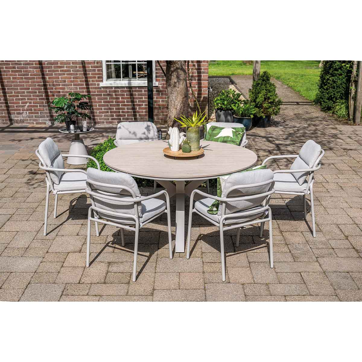 Round table with six chairs set around, with grey cushions. Brick wall in the background.