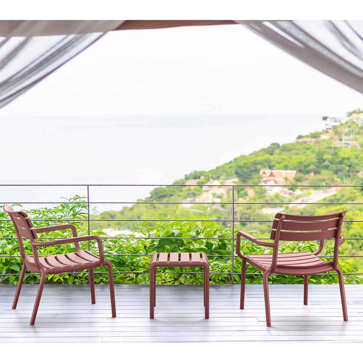 Two pink chairs and a matching table on a balcony, with a sea view.