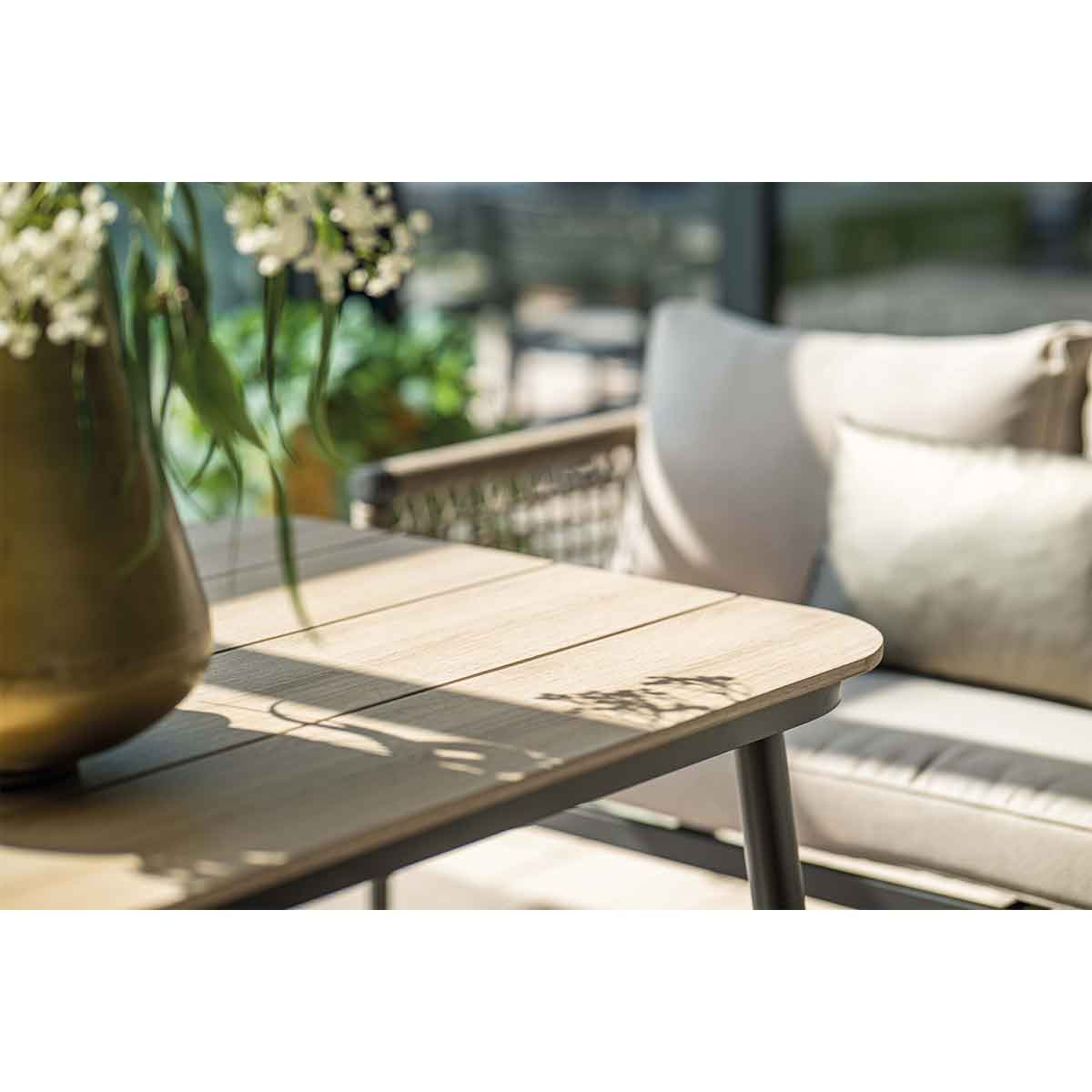 Gros plan sur une table en bois avec un vase de fleurs, montrant la lumière du soleil et les ombres.