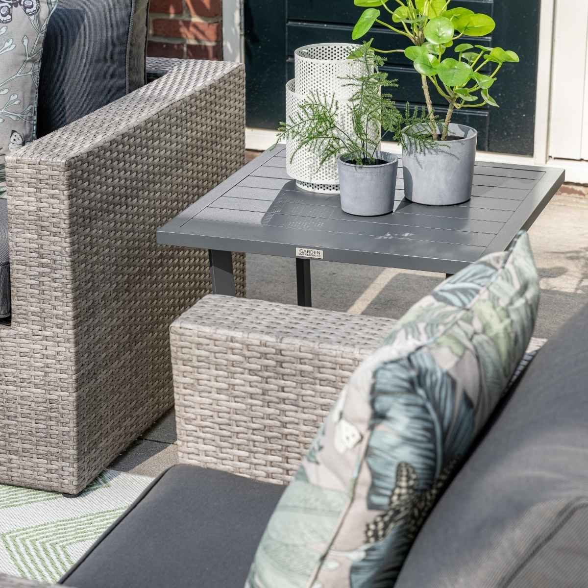 Une table grise avec des plantes, une chaise et un canapé en osier.