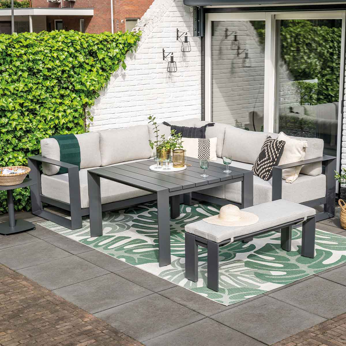 Un ensemble de patio extérieur avec des meubles gris, une table et un tapis vert.