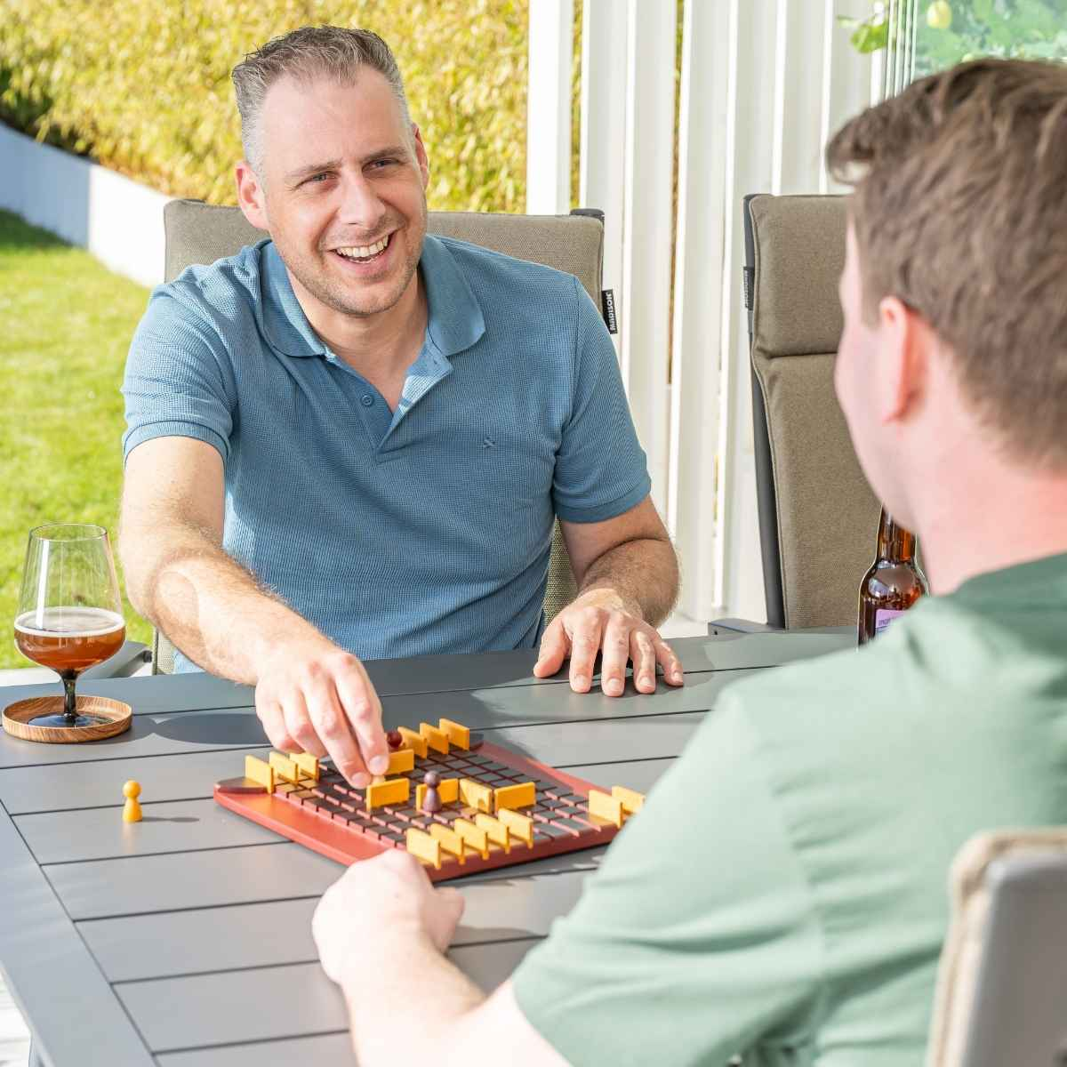 Two men playing a board game on a table with a glass of beer. Green background.