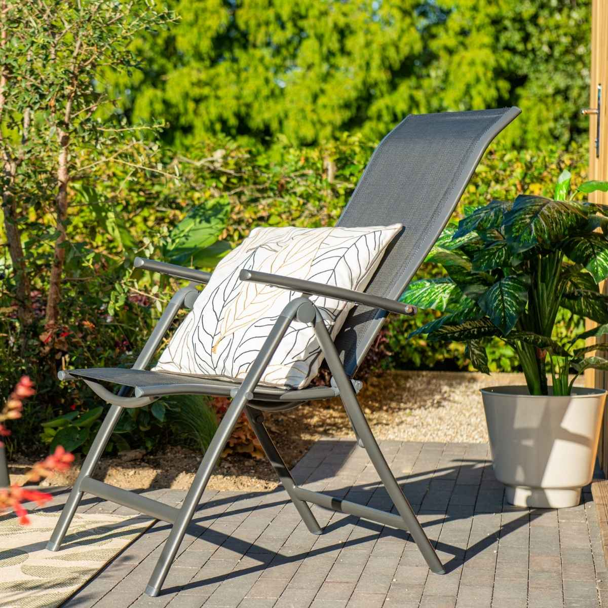 Folding chair with a pillow. Green bushes and plants in the background. Wooden floor.