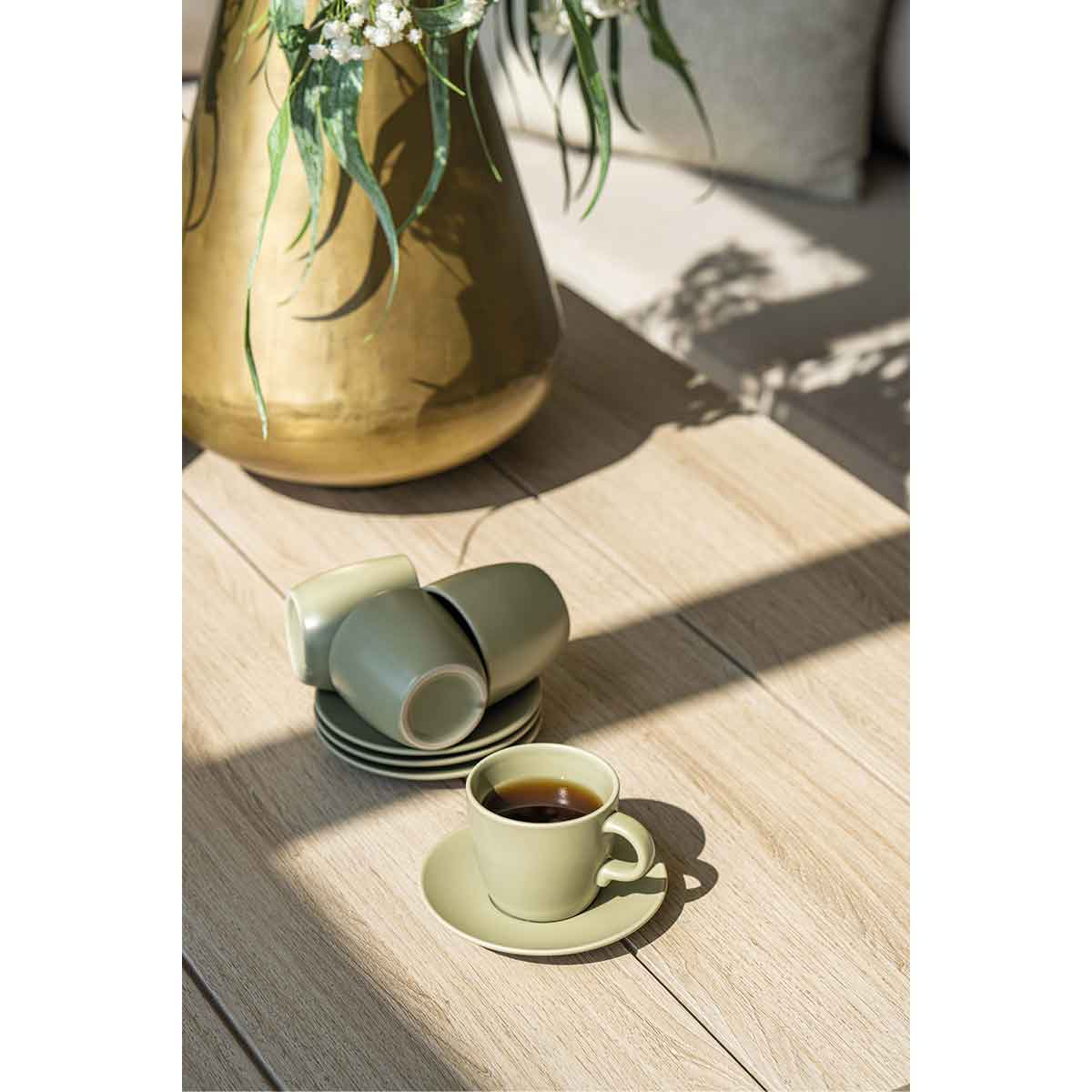 Tasses à café sur une table en bois. Tasses vertes, soucoupes et un vase doré derrière.