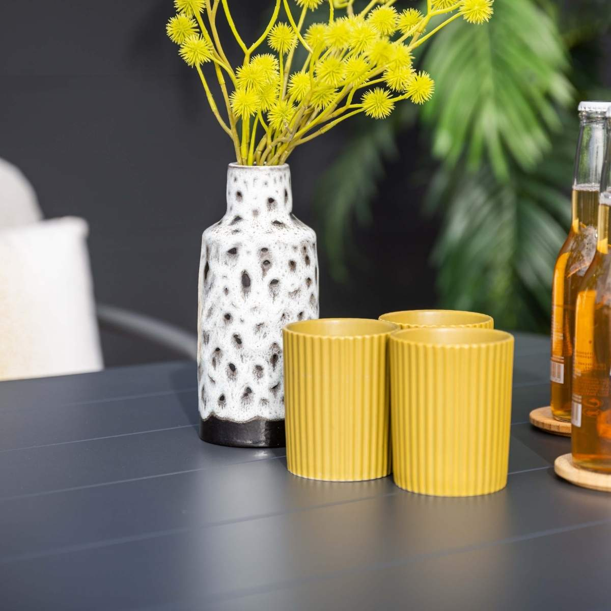 Gros plan d'une table avec des fleurs jaunes dans un vase, des tasses jaunes et des bouteilles de bière.