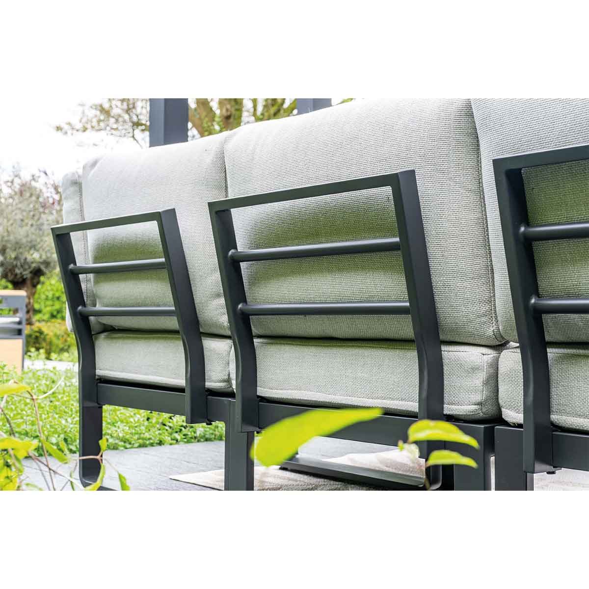 Close-up of the back of a gray sofa with a green leaf in the foreground.