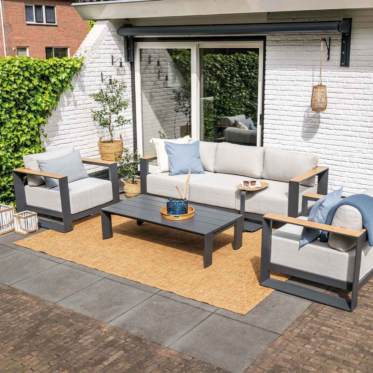 Buitenwoonstel met een bank, twee stoelen en een salontafel. Er ligt een kleed op het terras.