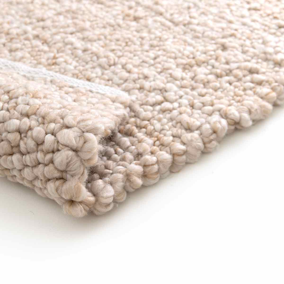 Close-up van beige tapijt met opgerolde rand die de onderkant laat zien.
