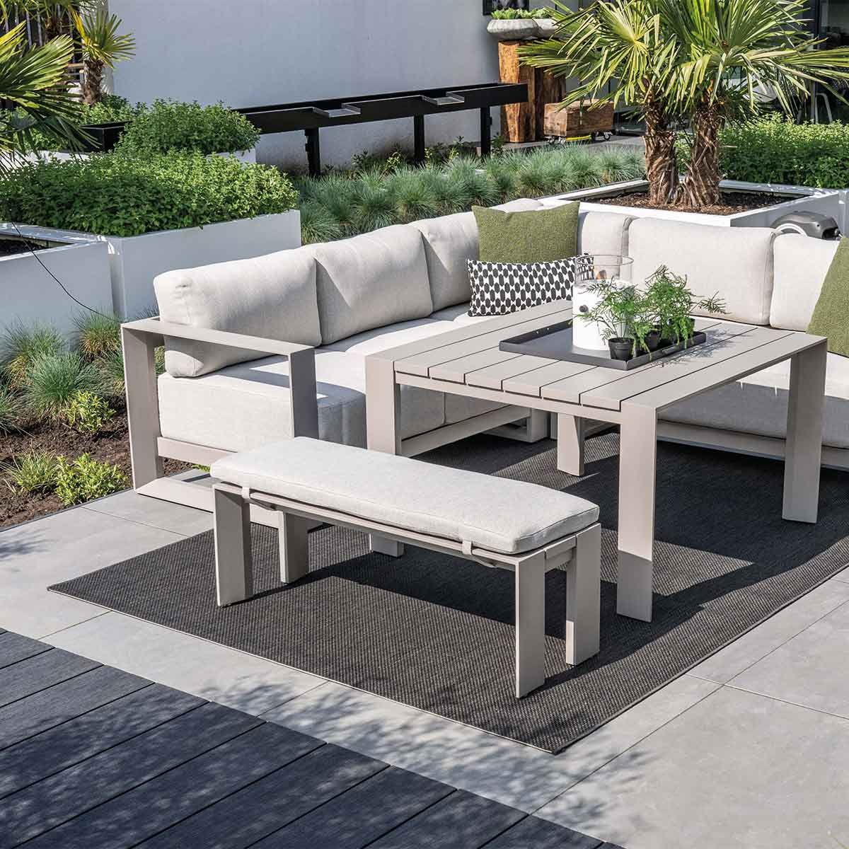 Coin salon extérieur avec mobilier gris, plantes et tapis. Jour ensoleillé.