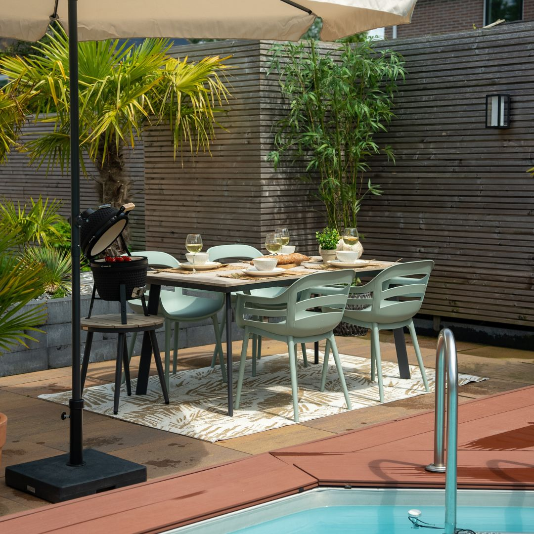 An outdoor dining set with a table, chairs and an umbrella. The setting is near a pool.