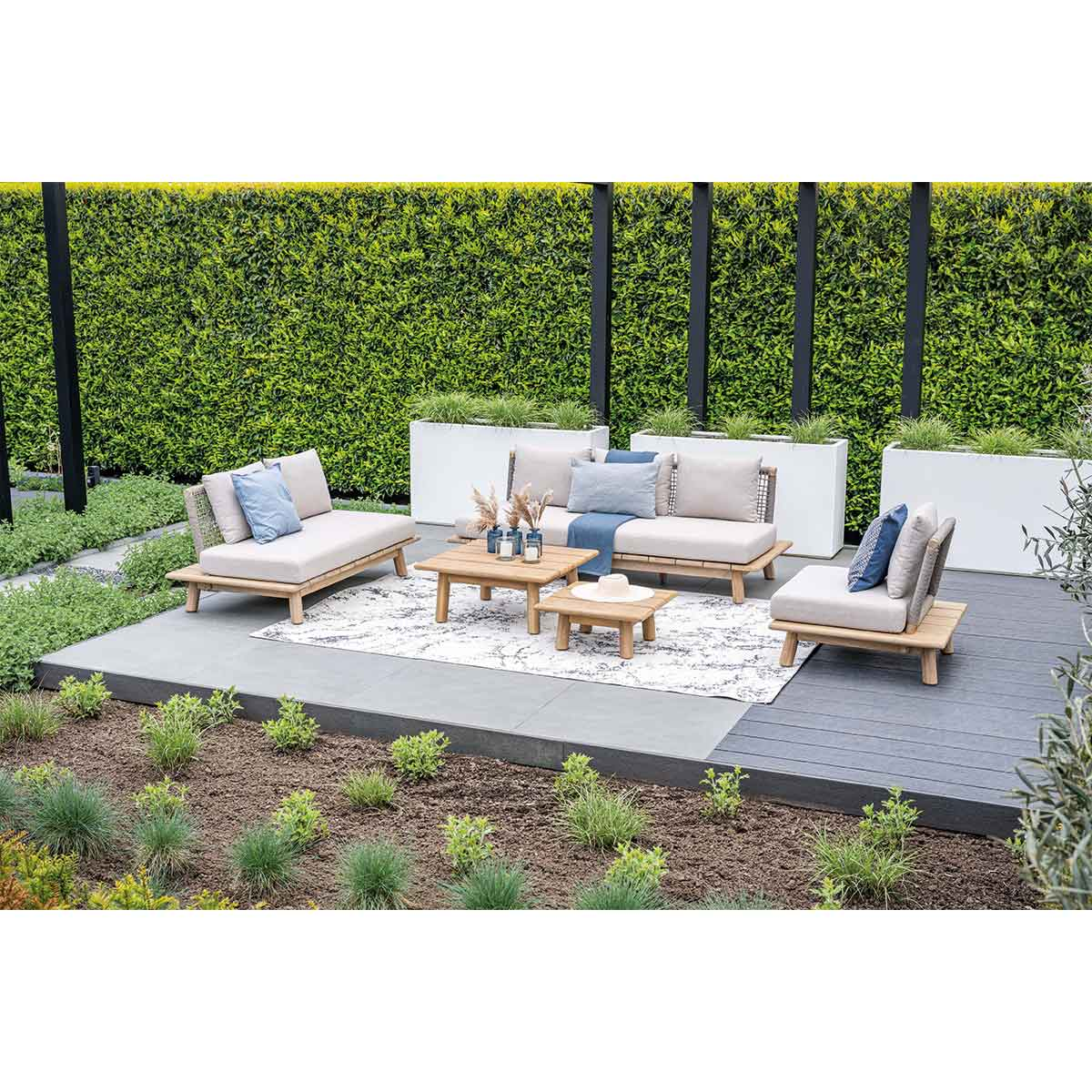 Outdoor patio furniture with a green hedge background and a wooden deck.