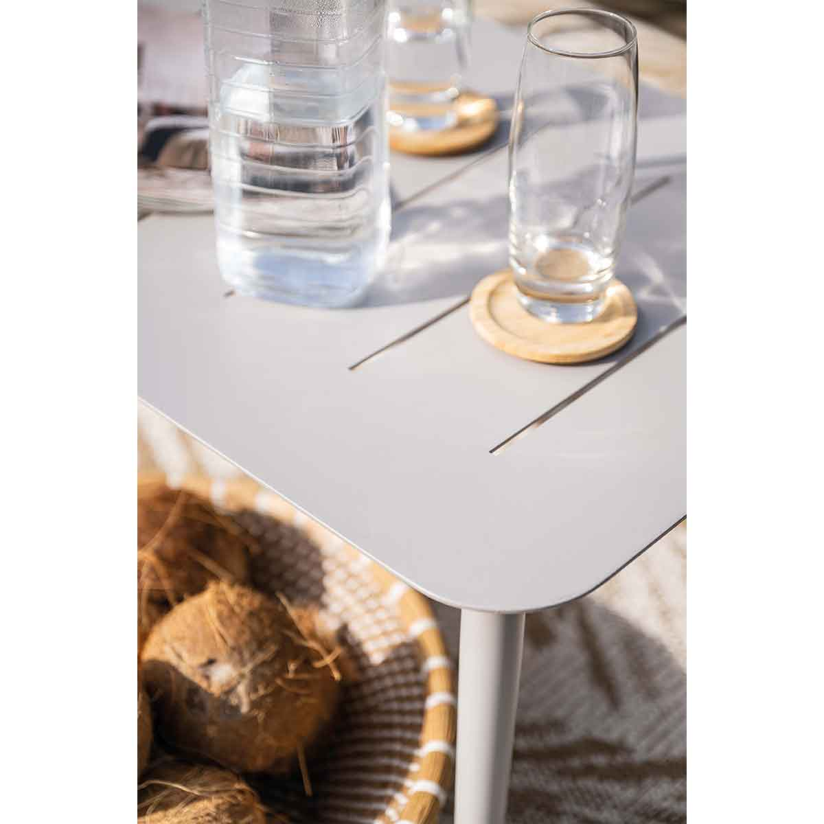 Close-up of a grey table with two glasses of water and some coconuts. Wood coasters present.