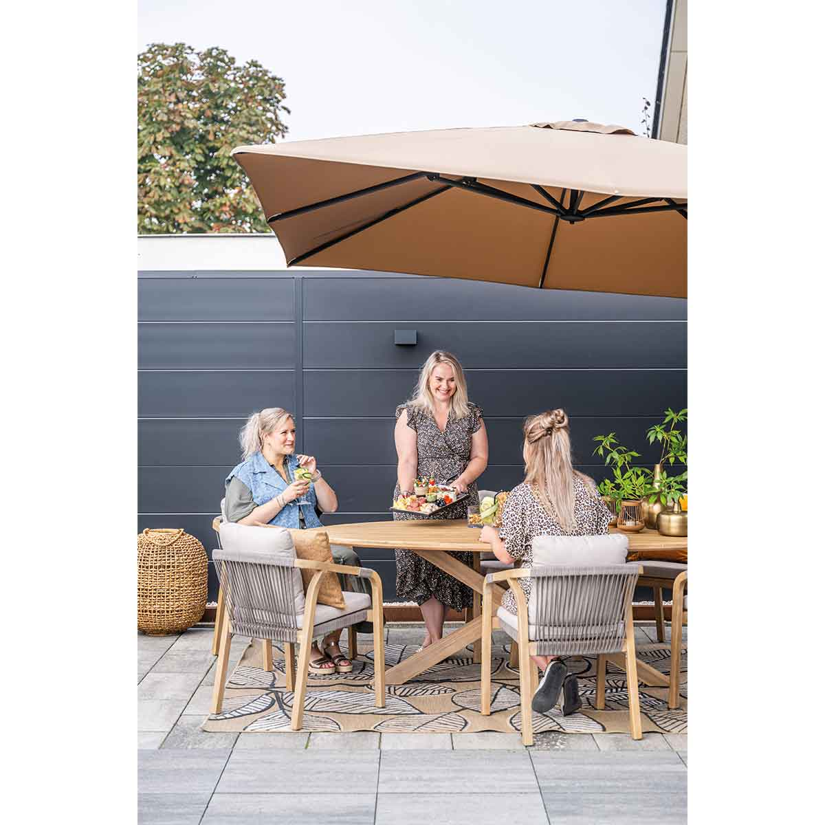 Three women at a table under an umbrella, enjoying drinks and snacks in an outdoor setting.
