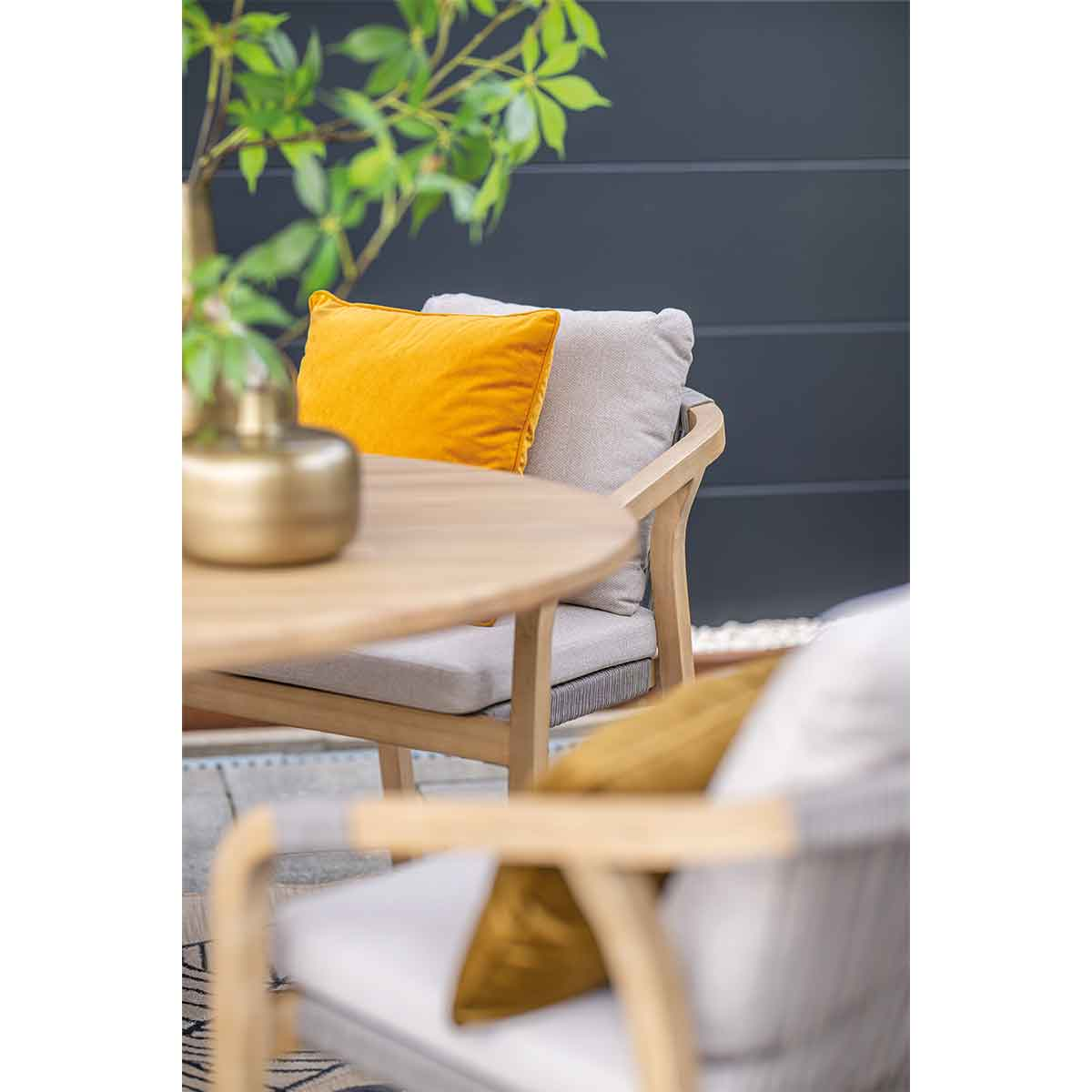 A table setting with a yellow pillow, chair, and a golden vase. Blurred background.