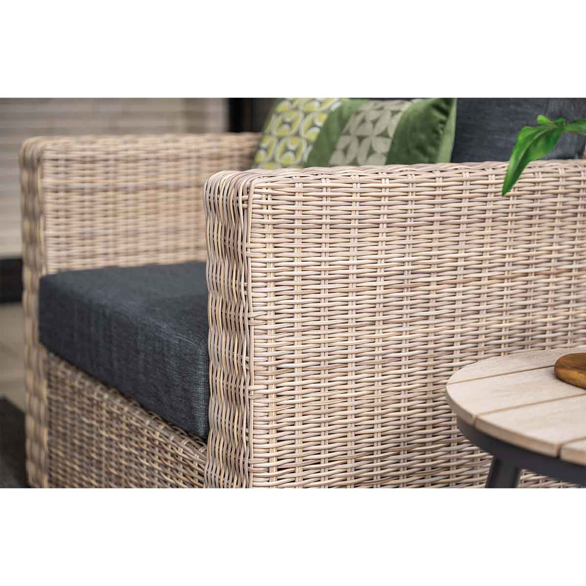Gros plan sur une chaise d'extérieur tissée. Coussin gris visible, osier beige.