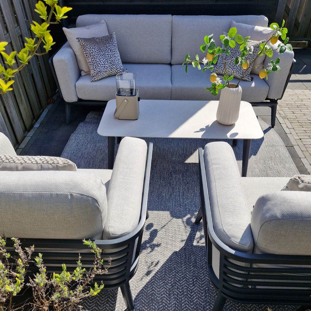 Buiten zithoek met bank, stoelen en tafel, citroenboom en planten.