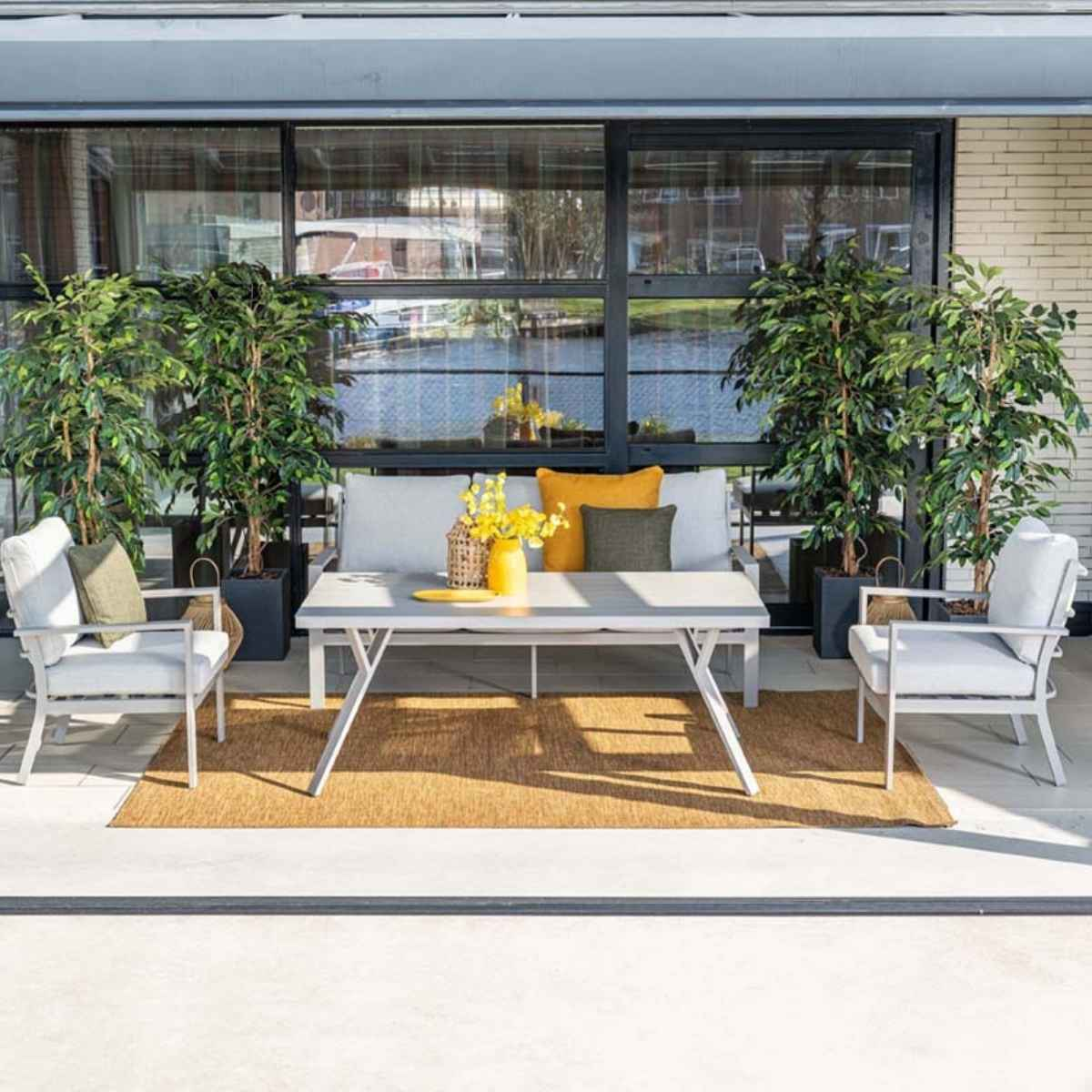 Un ensemble de patio extérieur avec des meubles gris, des plantes et une porte vitrée en arrière-plan. Table, chaises, canapé.