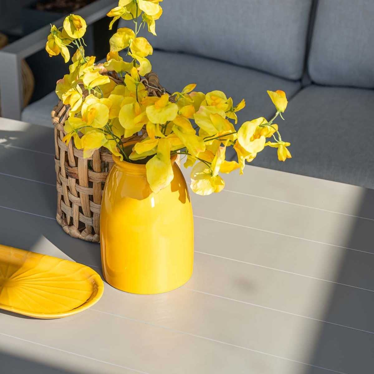 Fleurs jaunes dans un vase, un panier tressé et un plateau jaune sur une table grise.