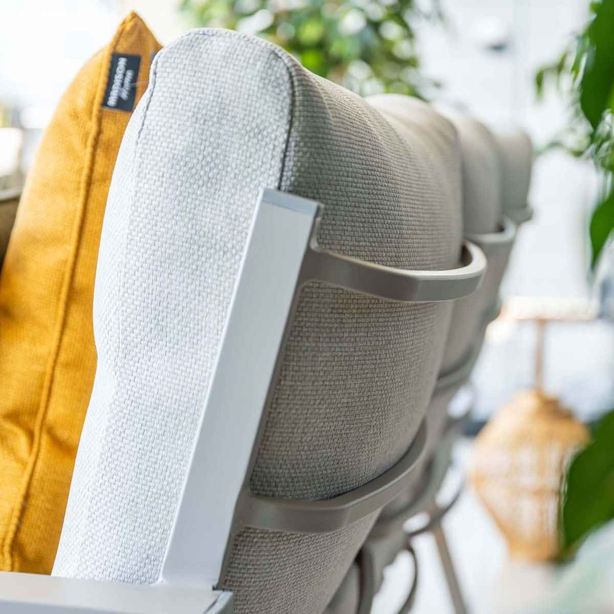 Dossiers de chaises grises d'extérieur avec coussin et oreiller jaunes, avec des plantes vertes en arrière-plan.