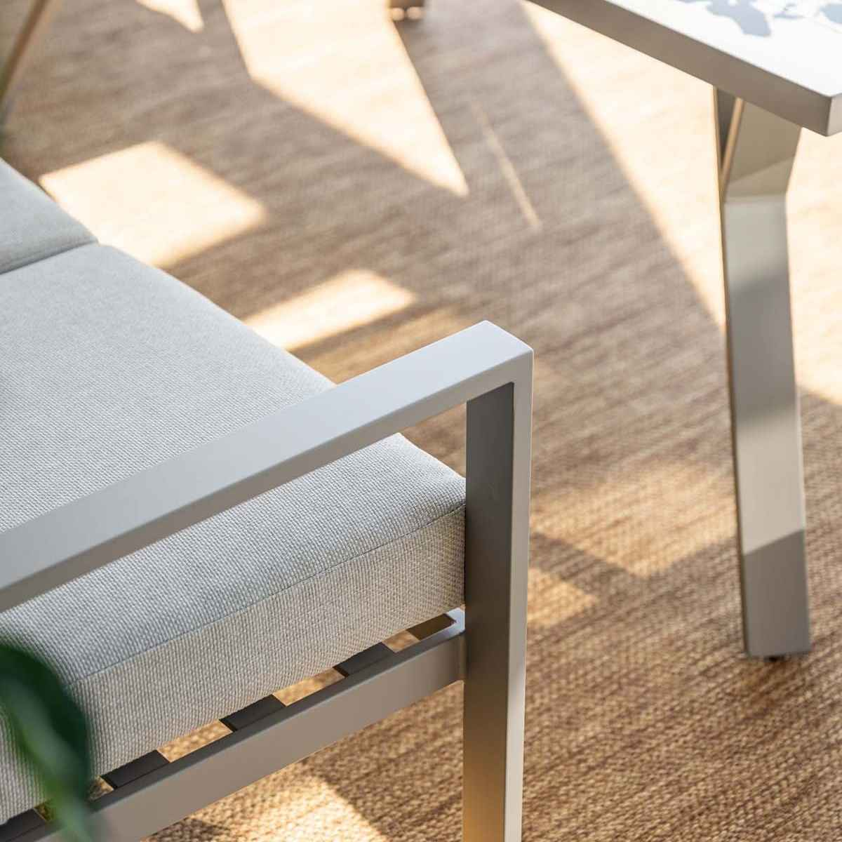 Gros plan sur l'accoudoir d'un canapé extérieur gris. Le canapé est sur un tapis marron.
