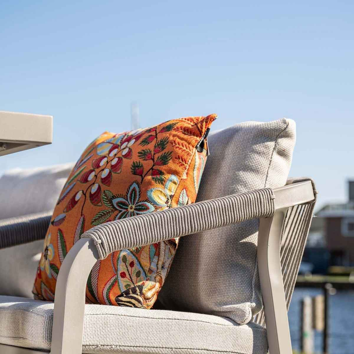 An orange floral cushion on a gray outdoor chair armrest with a blue sky background.