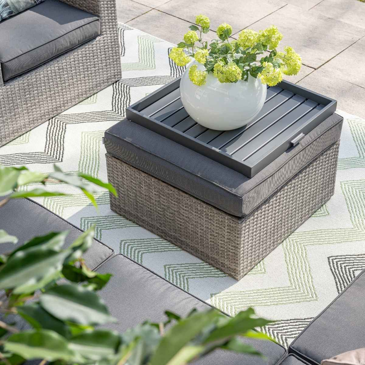 Rieten poef met dienblad, planten en vloerkleed. Bank in de hoek.