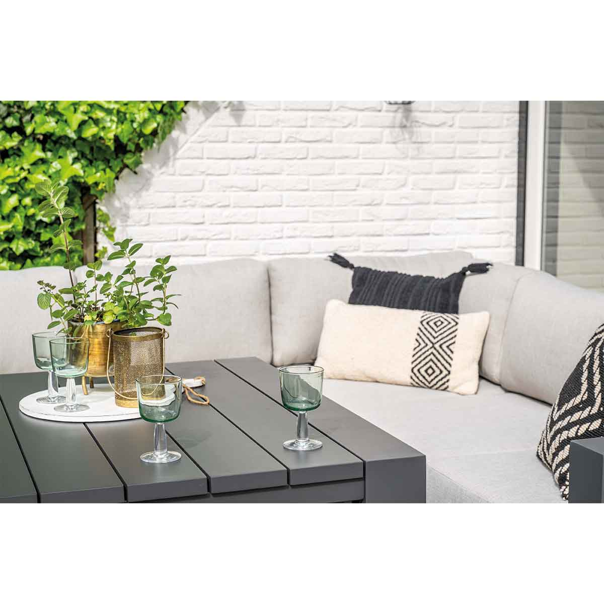 Buitenmeubelset: bank, tafel, planten en glazen. Witte bakstenen muur op de achtergrond.