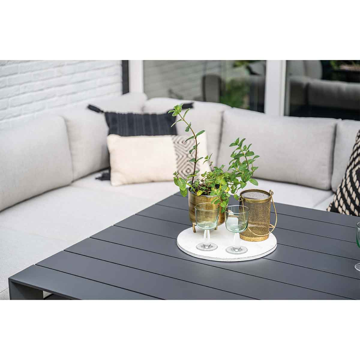 Tafelsetting met planten, glazen en kaarsen op een terras. Bank op de achtergrond.