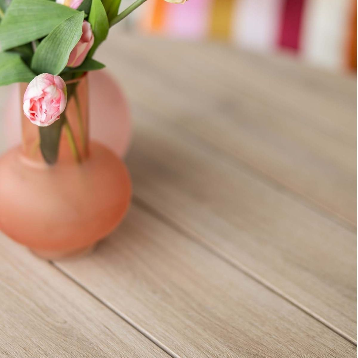 Close-up van roze tulpen in een vaas op een houten tafel met andere objecten.