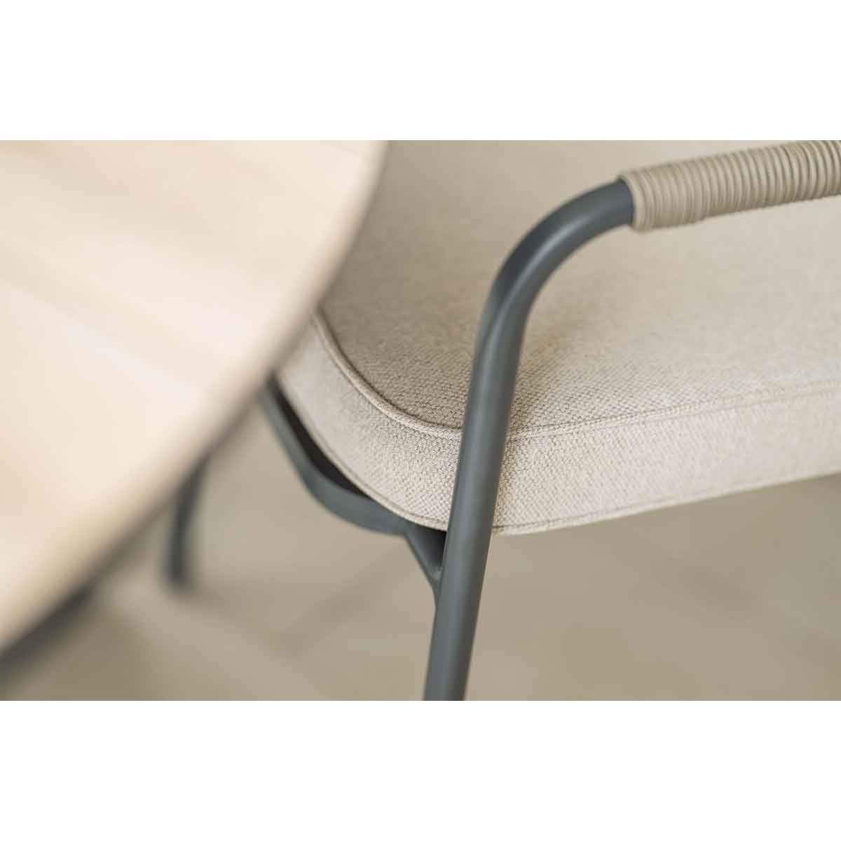Close-up of the armrest of a gray chair with a beige cushion on a light background.