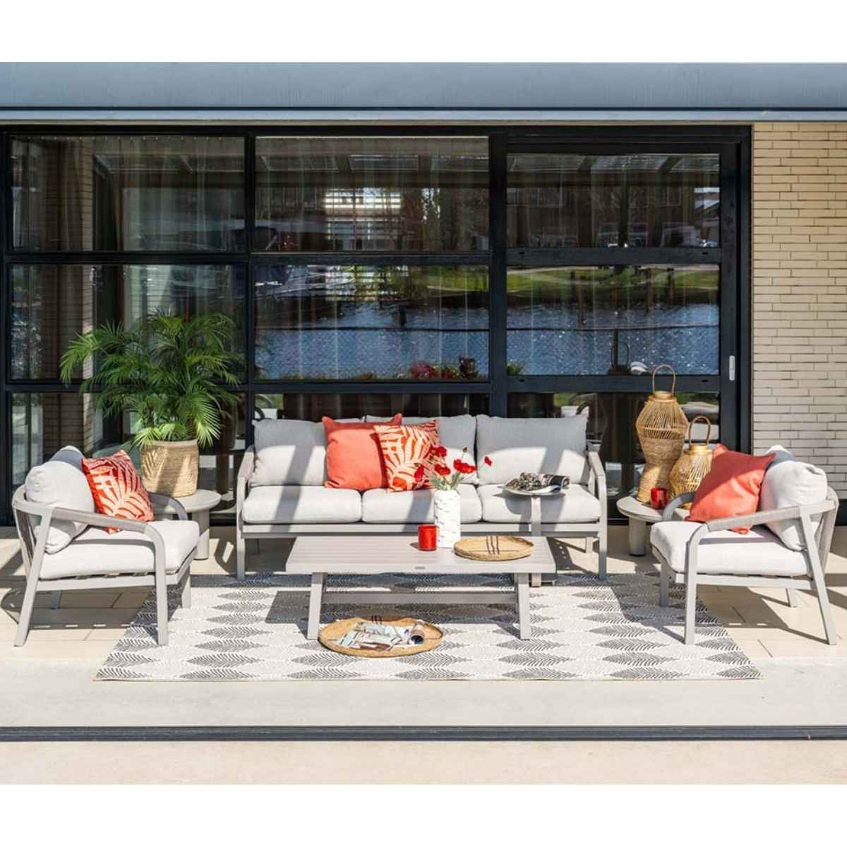 Outdoor patio furniture set. Gray sofa, chairs, and table. Rug and palm tree visible.