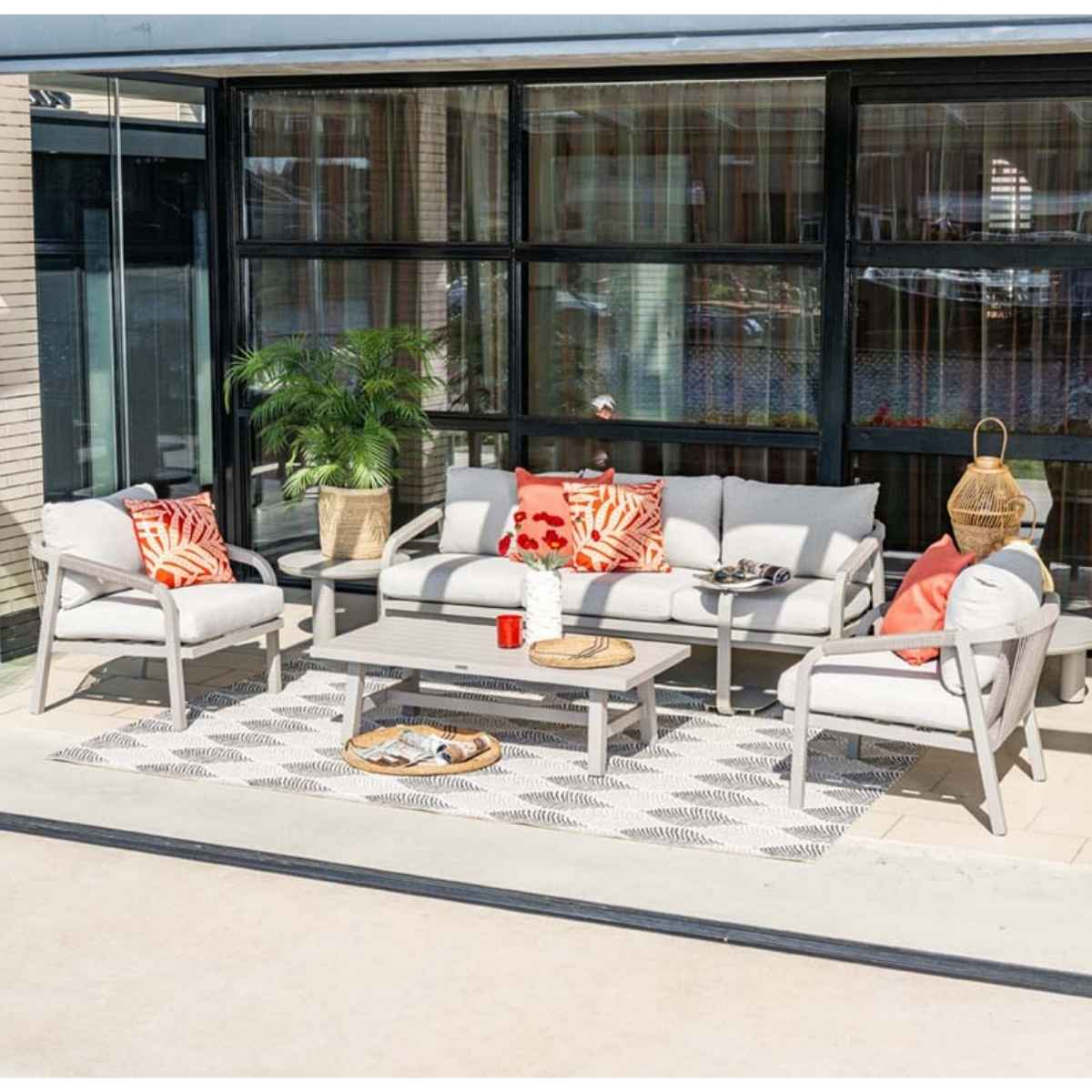 Outdoor living space with gray furniture, rug, and plants near a glass wall.