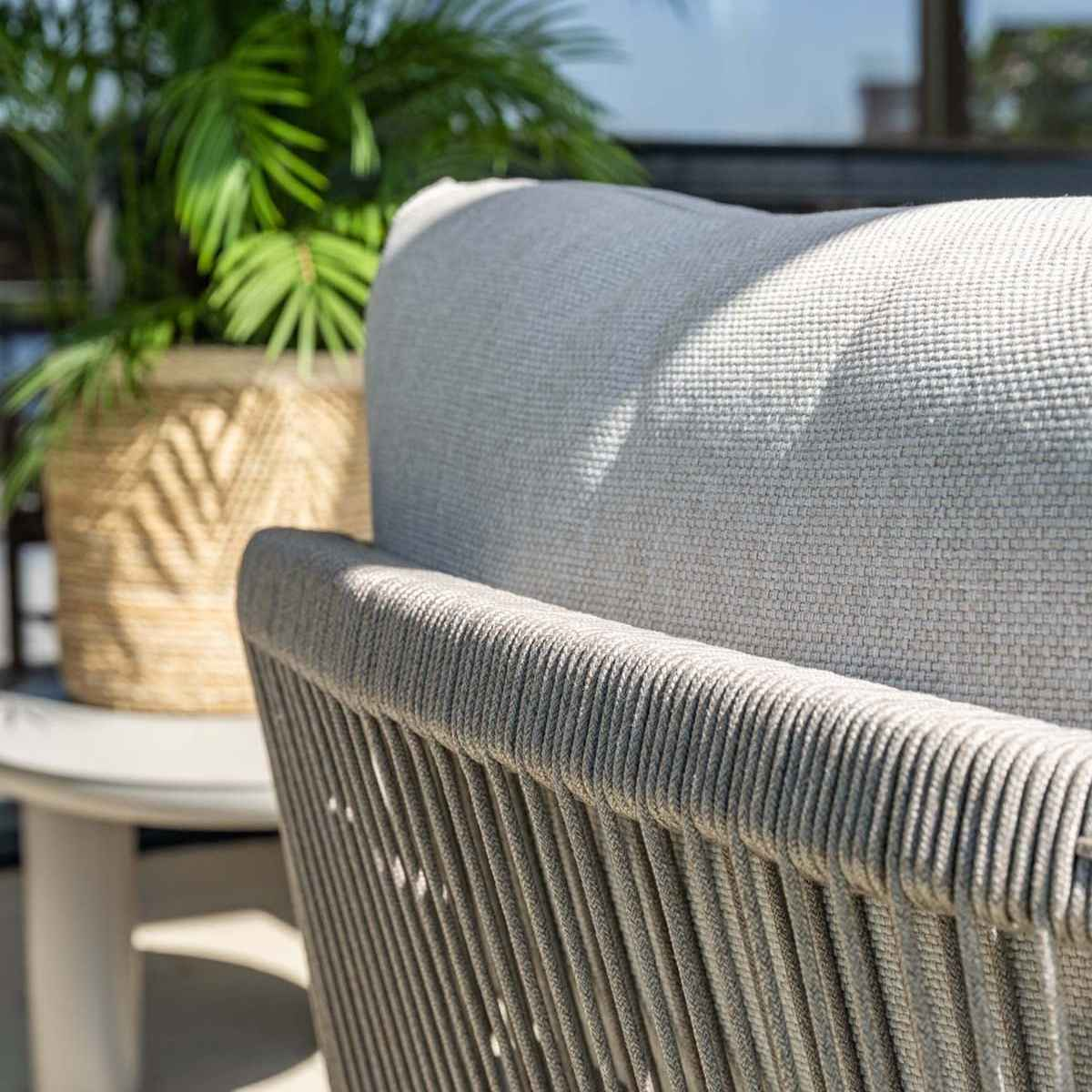 Close-up of the back of a chair with gray cushions and a woven rope frame.