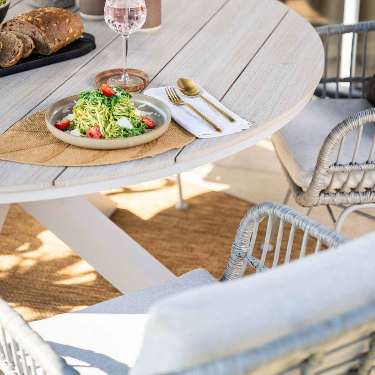 Outdoor table setting with pasta, bread, and drink. Includes a fork, knife, and glass of water.