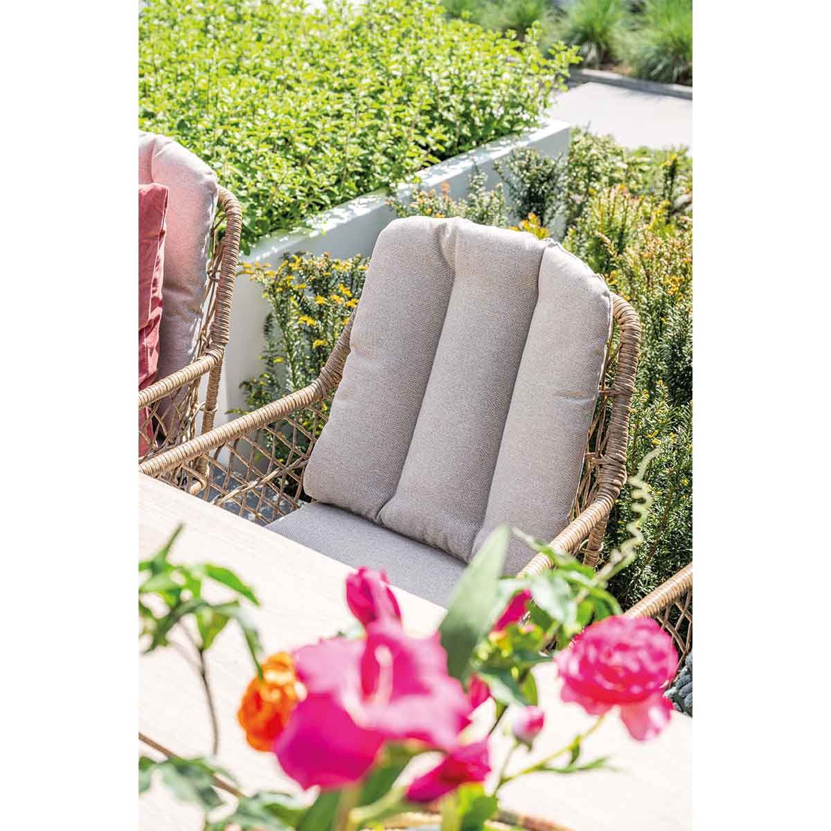 Close-up of an outdoor chair with a cushion. Flowers and greenery are in the background.