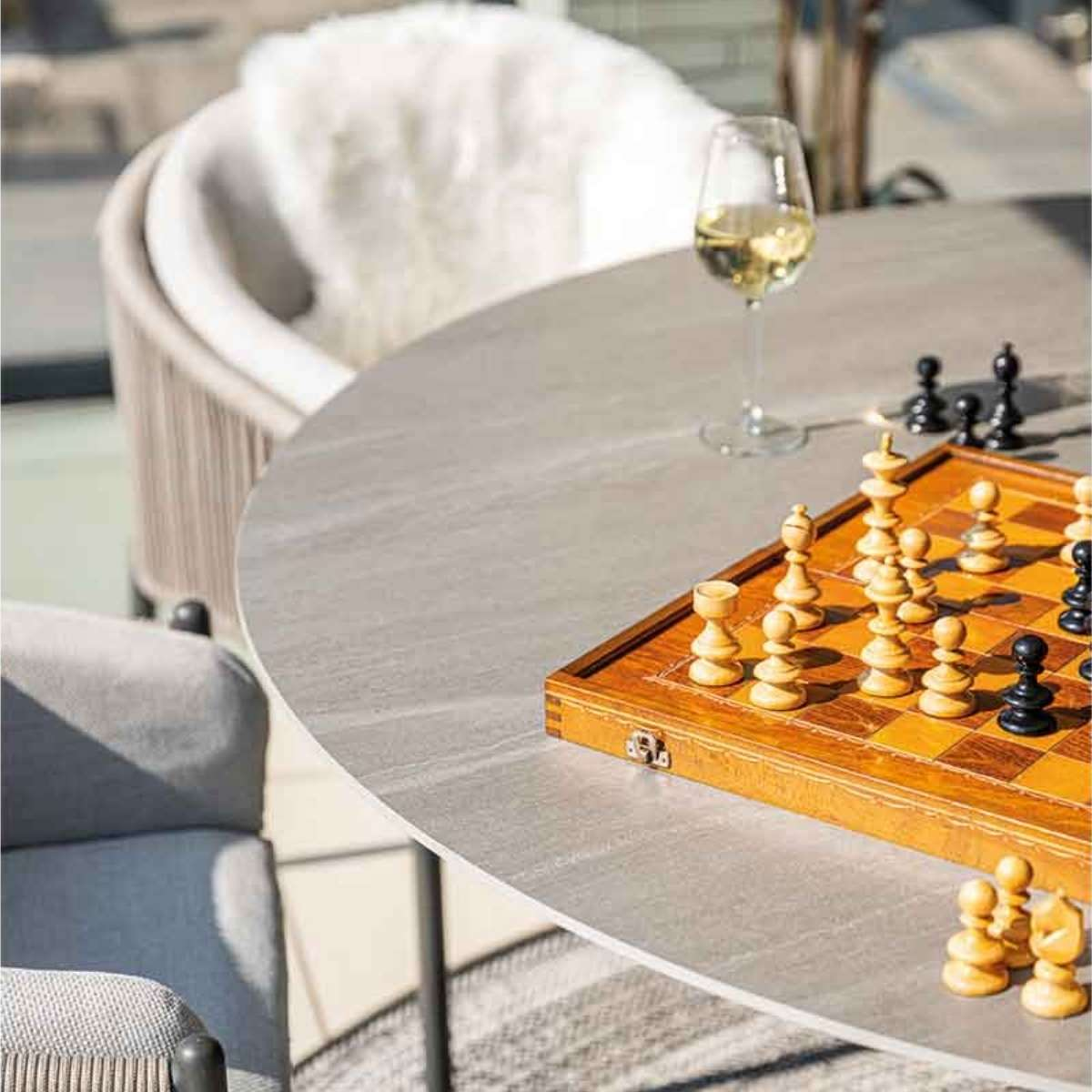 Schaakspel op een tafel, met een wijnglas en wat stoelen.