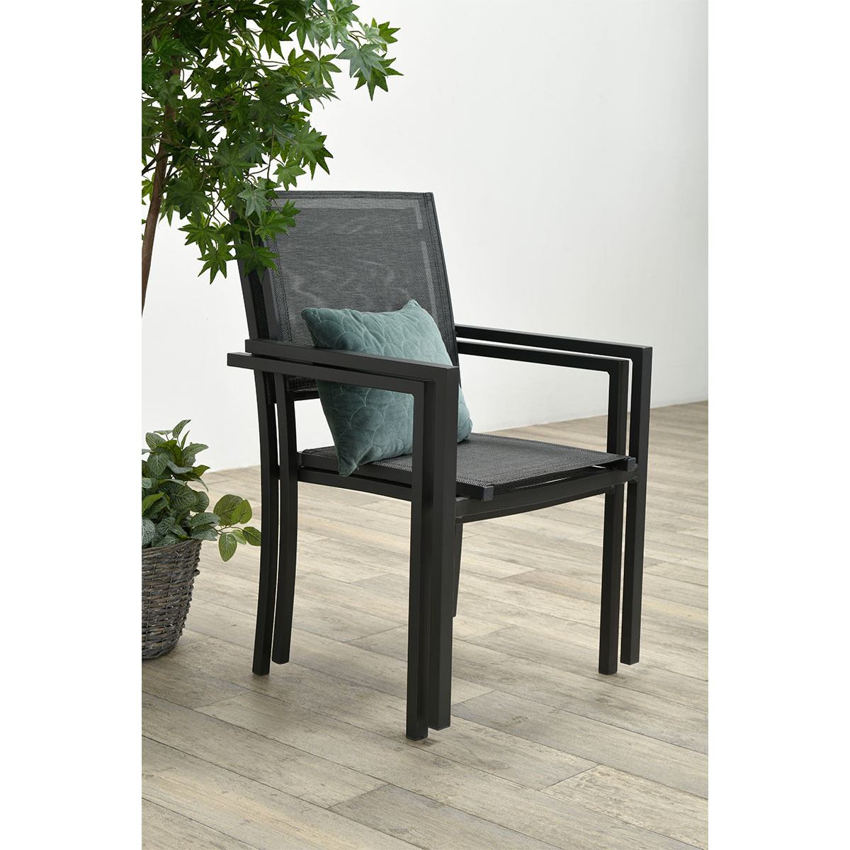 A black chair with a green cushion and a plant pot next to it. Wooden floor.