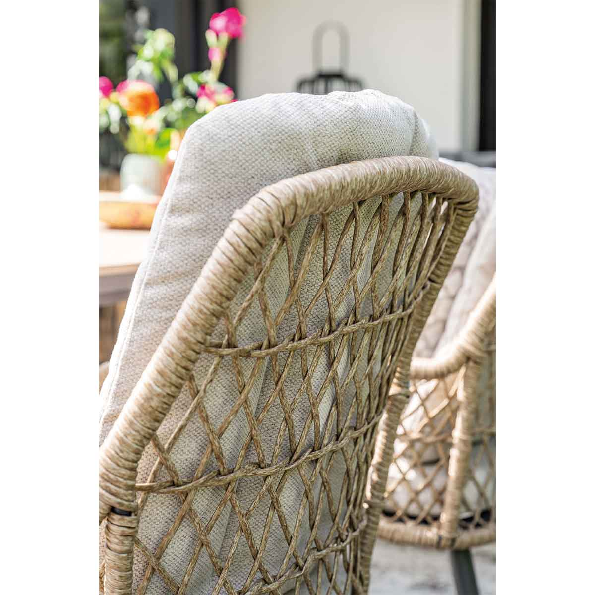 Gros plan du dossier de la chaise en rotin. Coussin gris clair. Fleurs floues en arrière-plan.