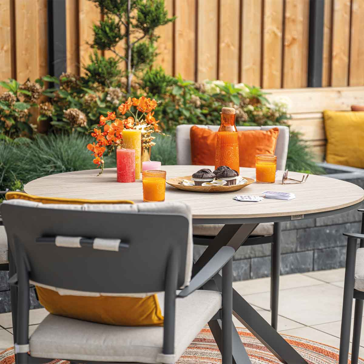 Outdoor table setting with drinks, candles, and food.  Backdrop includes a fence and plants.