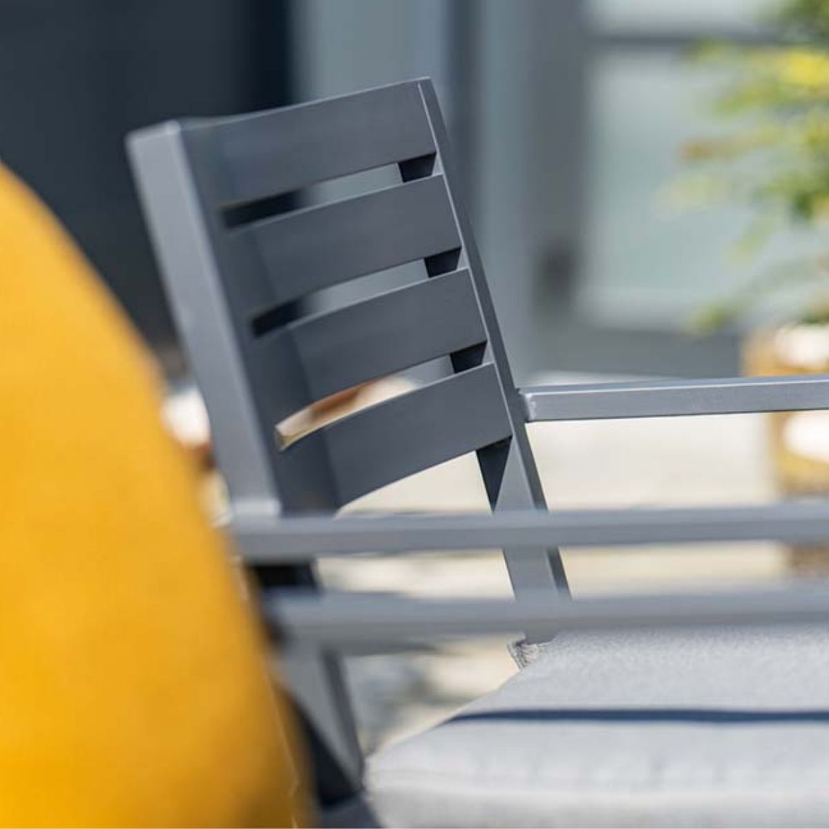 Close-up of outdoor chair. Gray frame with a yellow cushion. Green background.