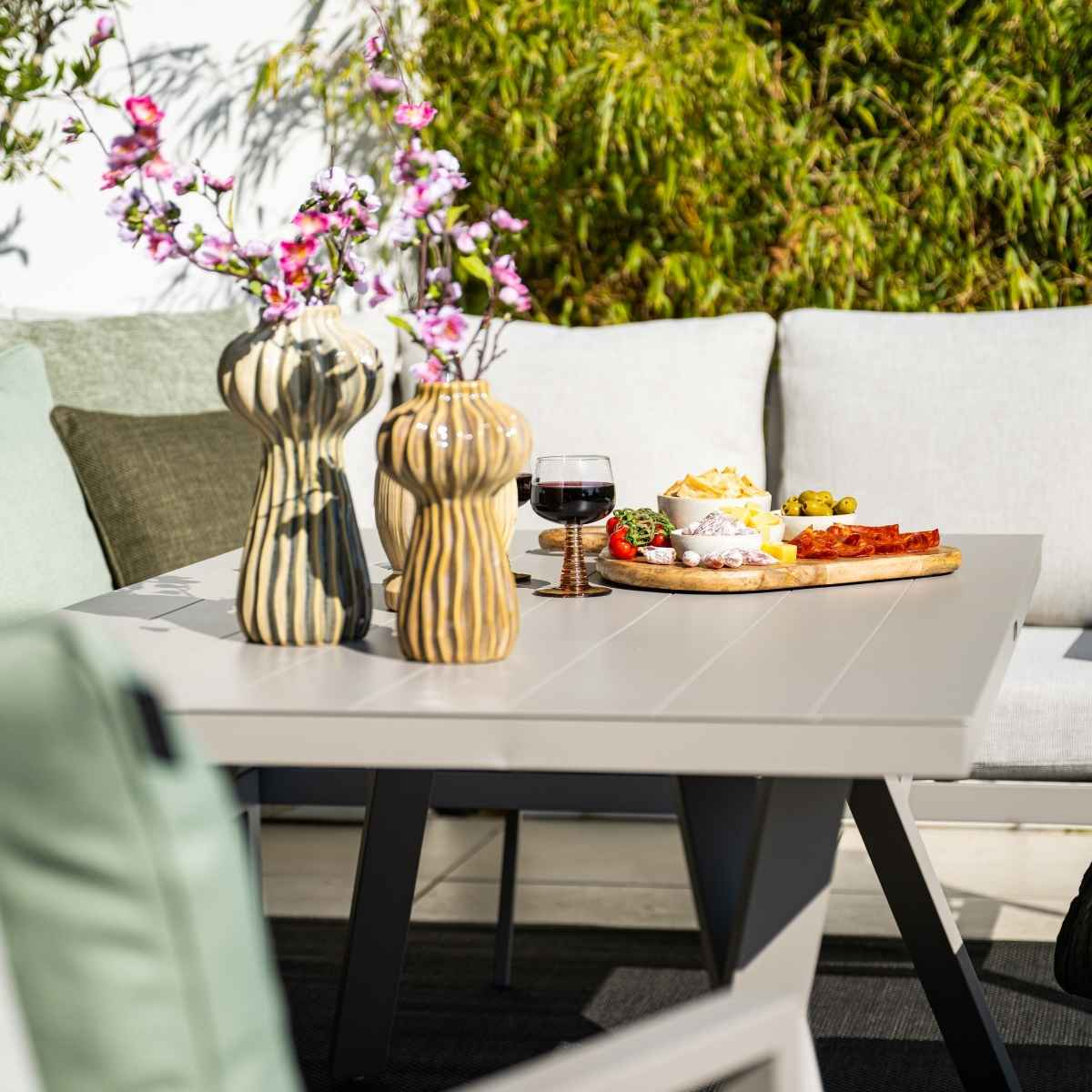 Table avec nourriture, boissons et fleurs sur un patio, avec un canapé et des plantes.